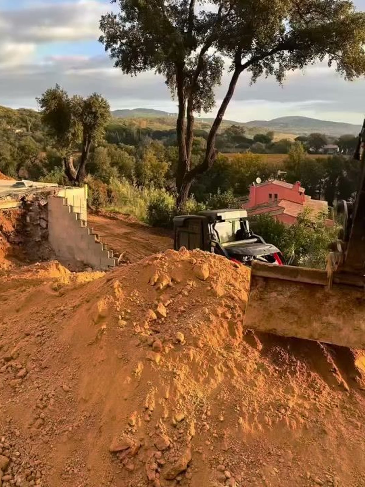 Terrassement en cours : pelle mécanique, terre décaissée et mur de soutènement en agglos
