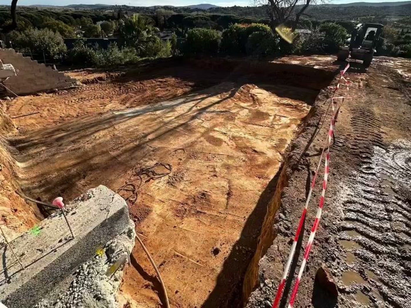 Fouille de terrassement ouverte, rubalise et mur en agglos, collines du golfe en arrière-plan